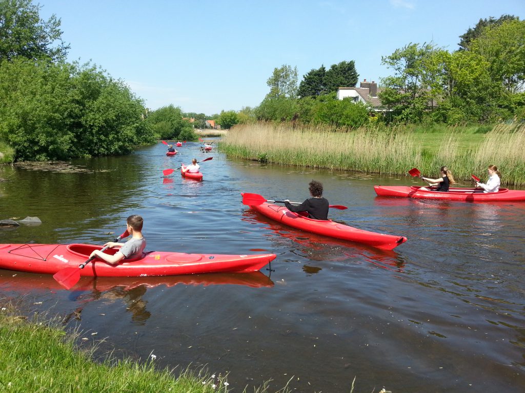 De groep neemt een ontspannen pauze tijdens het kanovaren, wachtend op de rest, genietend bij De Klimvallei in Den Helder. Kano's huren kan op de website.
