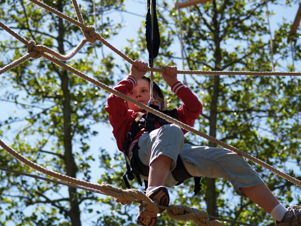 Spannende klim: kind beklimt behendig een touwnet op aanzienlijke hoogte in De Klimvallei, Den Helder.