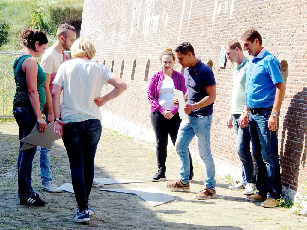 Groep deelnemers bezig met een tangram tijdens de Expeditie Robinson groepsactiviteit in Fort Kijkduin, Den Helder.